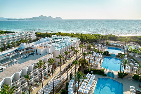 Luftaufnahme des Hotels Iberostar Selection Albufera Playa. Links im Bild sieht man die Zimmer und rechts ist ein grosser, langer Swimmingpool umsäumt von Palmen zu sehen. 