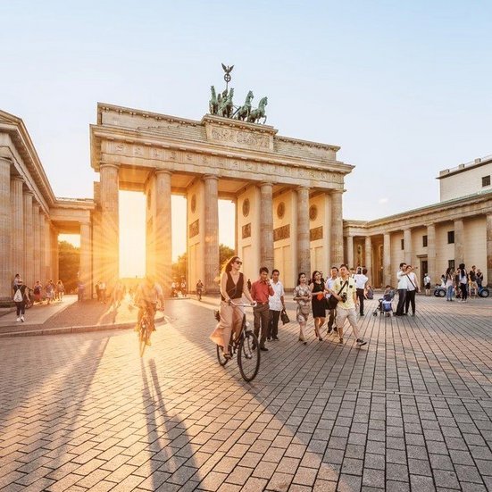 Brandenburger Tor in Berlin, Deutschland, bei Sonnenuntergang, umgeben von Menschen und historischen Gebäuden.
