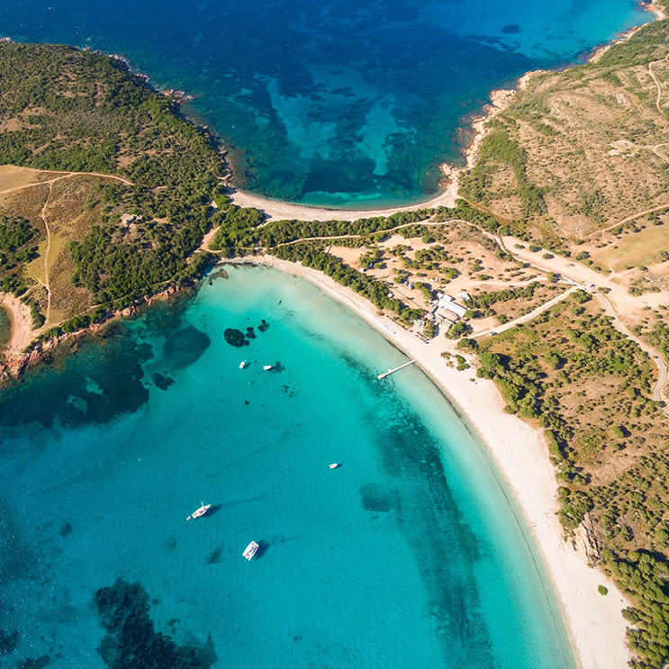 Aerial view von Korsikas Strand, wo das türkisfarbene Wasser sanft an den Sandstrand plätschert.